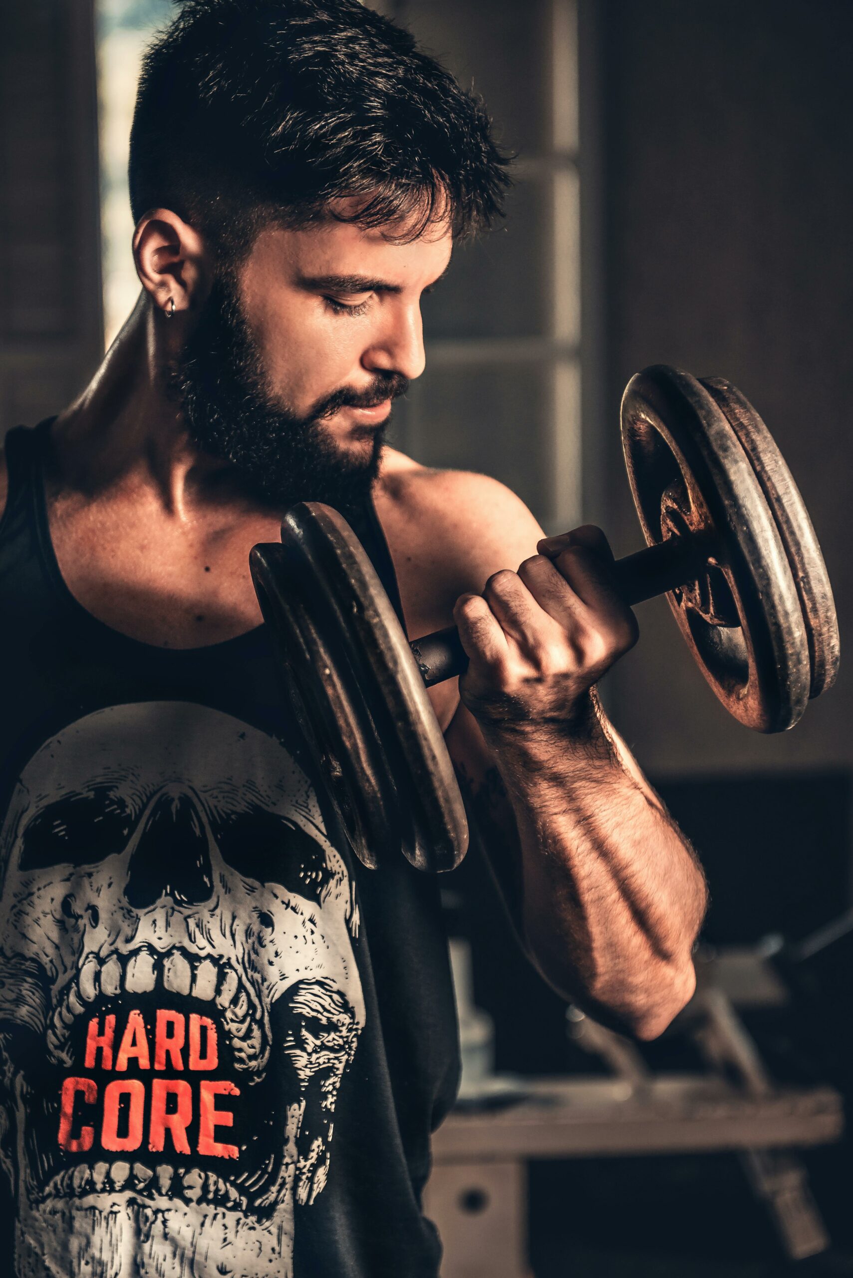 Bearded man in gym lifting a heavy dumbbell, showcasing strength and fitness.